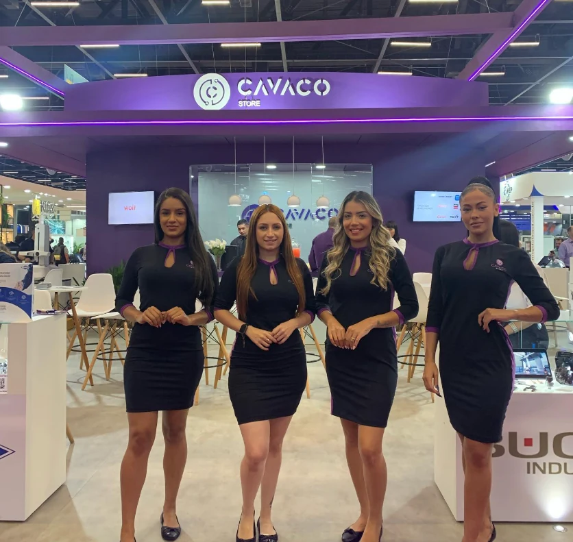 Quatro promotoras de vestido preto com detalhes roxos em frente ao estande da Cavaco Store na FEIMEC