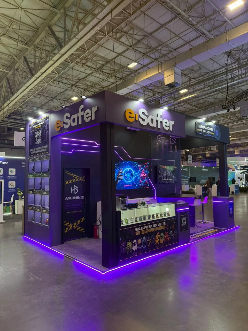Estande Laboratório de Ameaças da e-Safer no Mind The Sec 2026, com letreiros e-Safer e luz roxa no piso